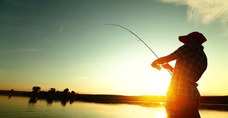man with fish on line inshore at sunset