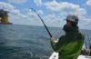 Young man on charter boat holding bent rod with fish on line