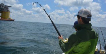 Young man on charter boat holding bent rod with fish on line