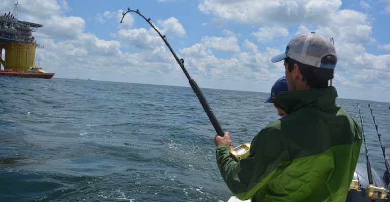 Young man on charter boat holding bent rod with fish on line